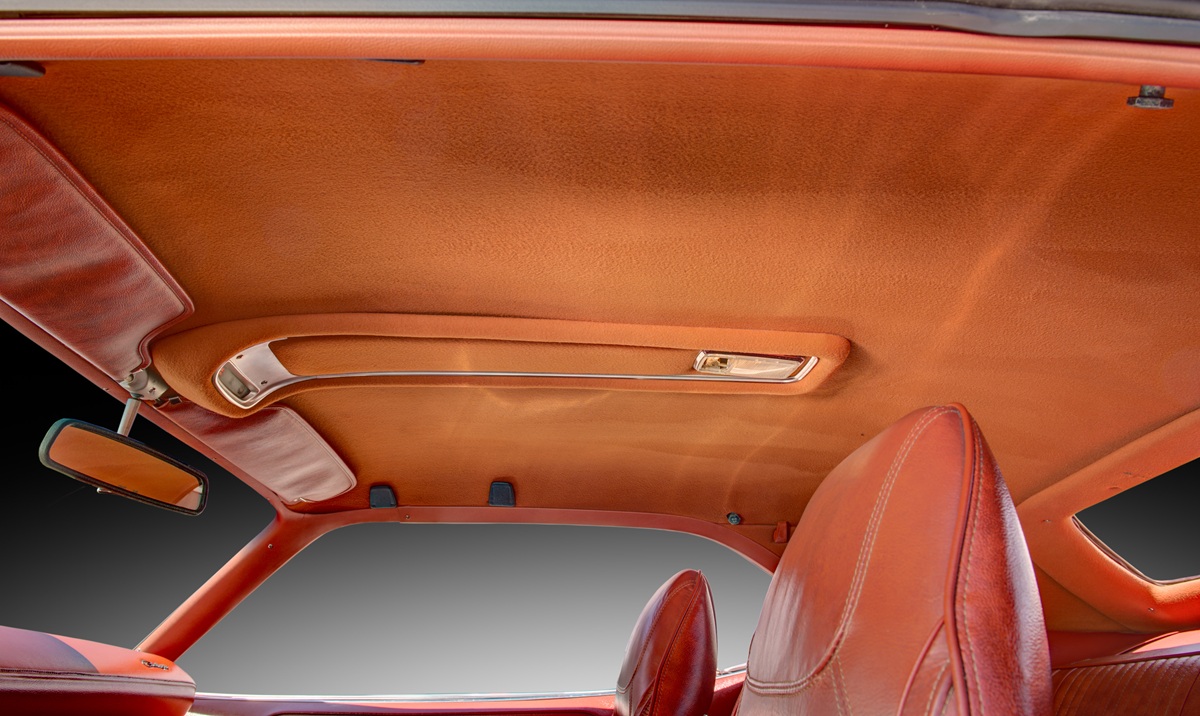 The image shows the interior roof and upper sections of a vintage car, featuring a brown headliner, interior light, rearview mirror, and two front seats with matching brown upholstery.