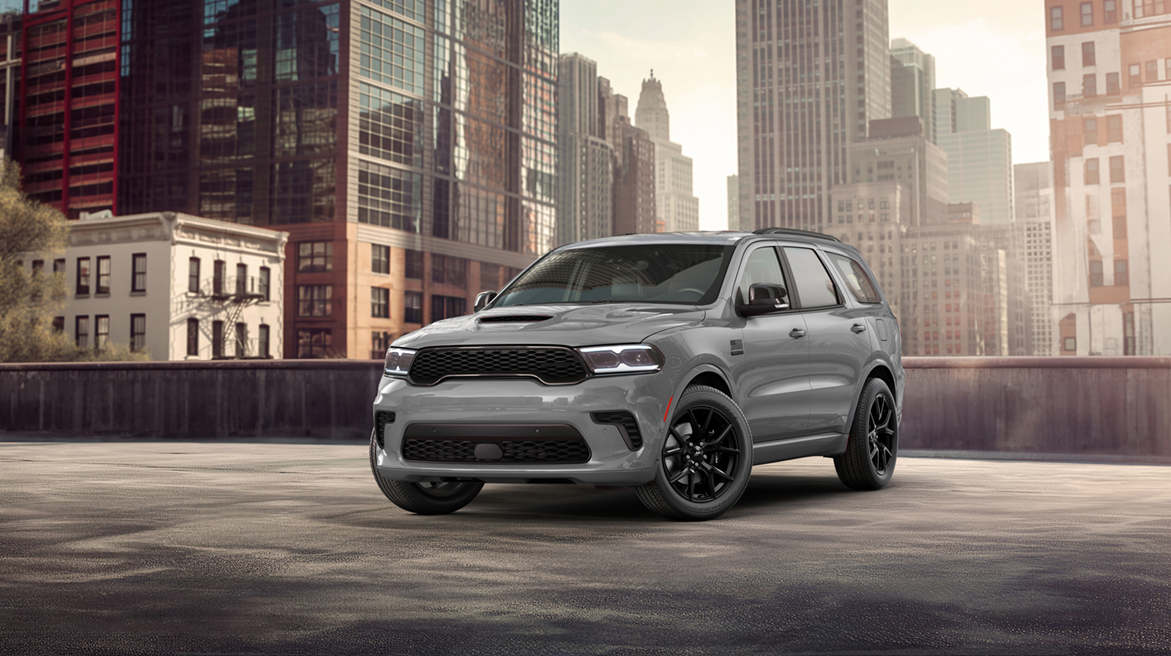 A gray durango with black wheels is parked on an empty rooftop with tall city buildings in the background under a partly cloudy sky.