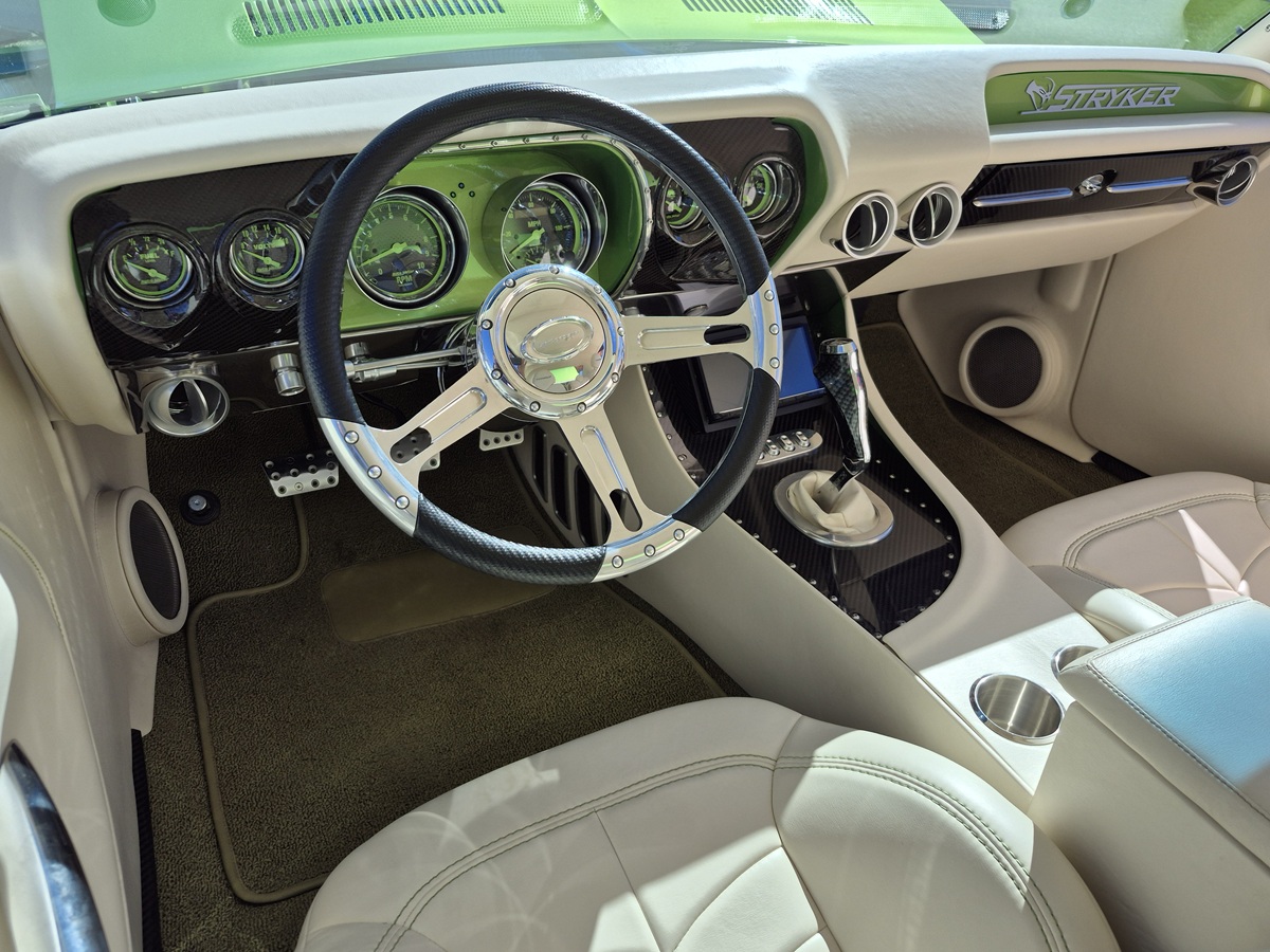Close-up of a cars modernized classic interior, featuring a metallic steering wheel, green-accented gauges, cream leather seats, and a clean dashboard with a Stroker badge. Sunlight highlights the sleek design.