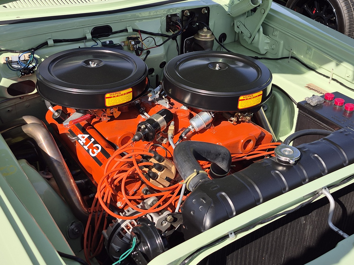 Bright orange V8 engine with dual black air filters and visible wiring in a vintage light green car’s clean engine bay. Labels show “413,” indicating engine displacement.