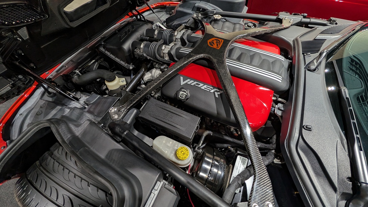 Close-up view of a Dodge Viper engine bay, featuring a red V10 engine cover labeled Viper and prominent carbon fiber cross brace, surrounded by various engine components and hoses.