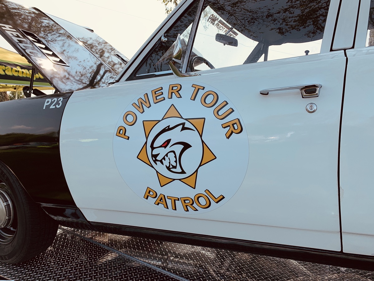 Close-up of a classic black and white car door with a large circular Power Tour Patrol emblem featuring a stylized animal face in the center and the text P23 on the front fender.