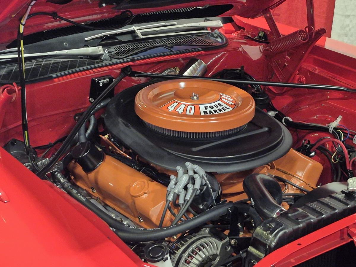 The image shows the engine bay of a classic red car, featuring an orange 440 Four Barrel V8 engine with visible spark plug wires and various engine components under an open hood.