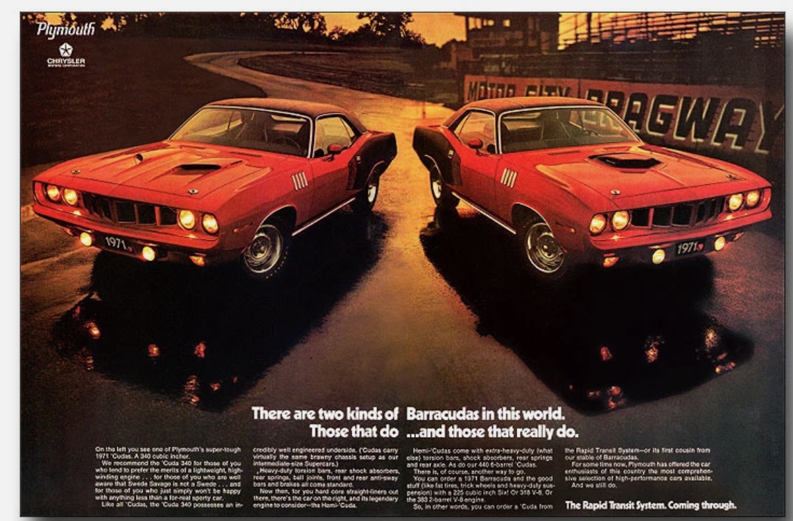 Two red 1971 Plymouth Barracuda muscle cars with headlights on are parked side by side at dusk on a racetrack, with a stadium and Raceway sign visible in the background.