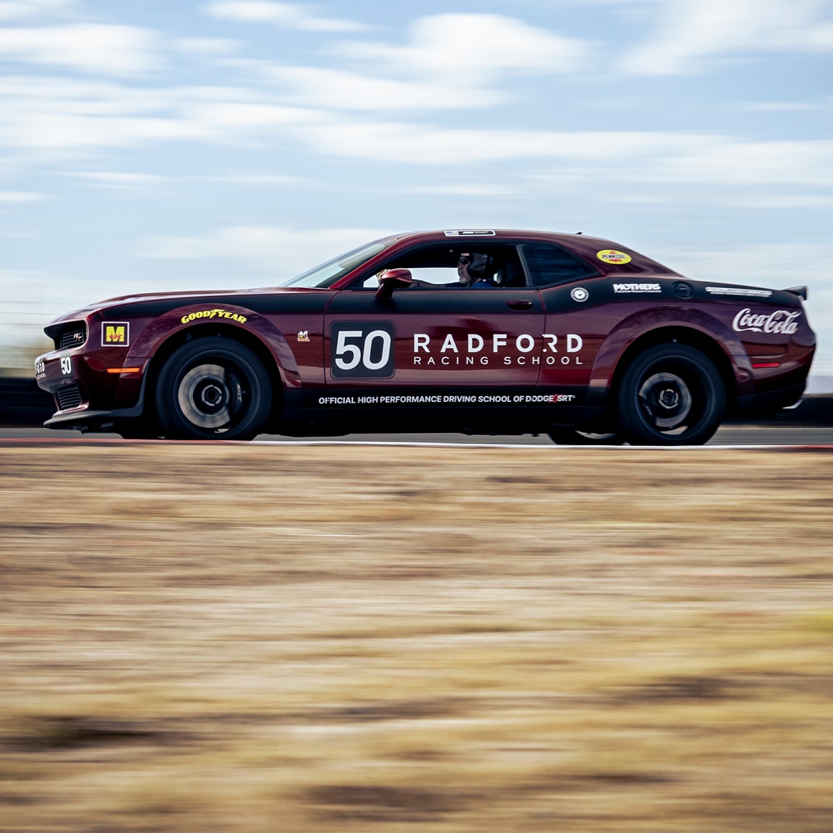 A maroon race car marked with the number 50 and Radford Racing School branding speeds along a track, with motion blur in the background and the wheels.