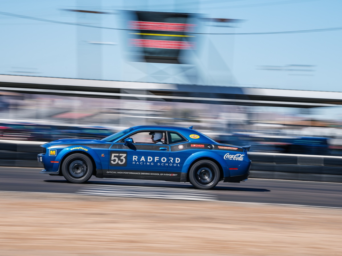 A blue Radford Racing School car with the number 53 speeds along a racetrack, motion blur in the background emphasizes its fast movement.