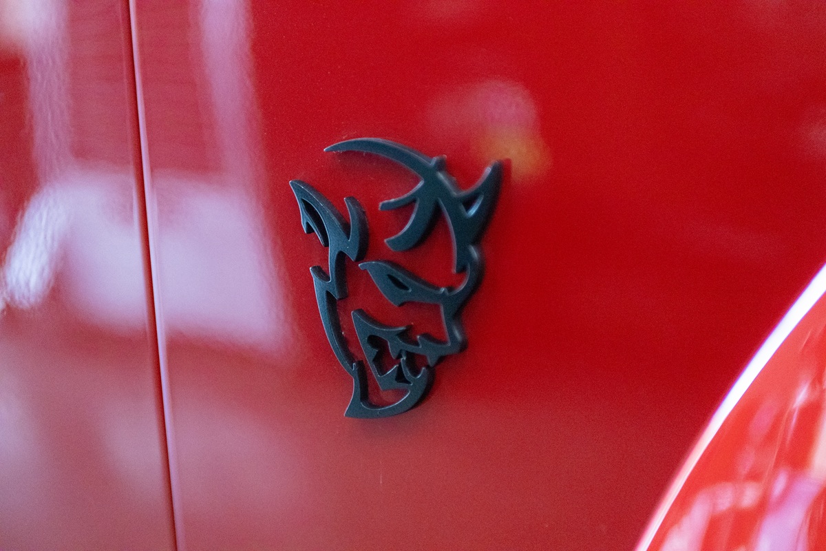 A close-up of a black demon head emblem on the shiny red exterior of a car.