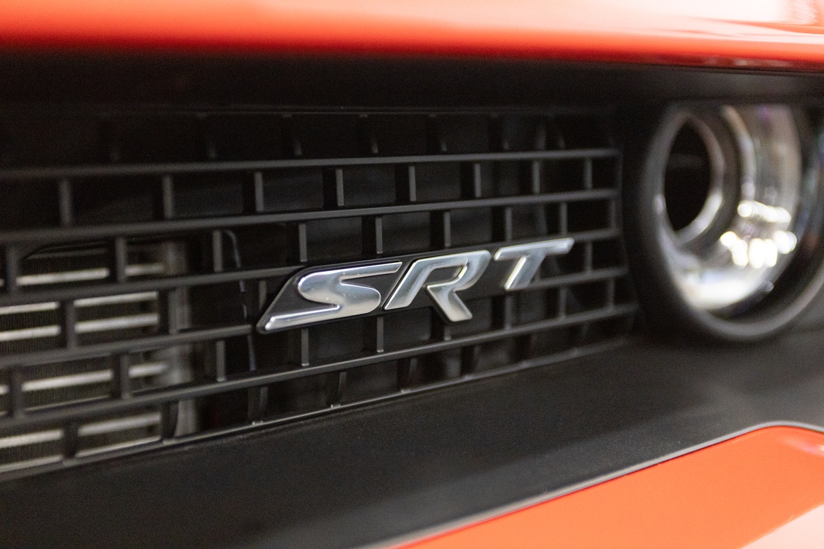 Close-up of a car grille with a metallic SRT badge in the center, bordered by an orange exterior and circular headlight detail visible on the right.